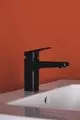 Schwarze Waschtischarmatur von Ideal Standard auf einem weißen Waschbecken, vor orangefarbener Wand. Der Wasserhahn hat ein schlichtes Design und ist mittig positioniert.